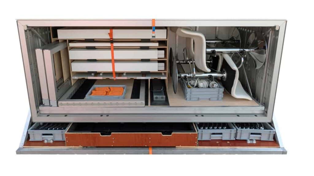 Beursstand Open metalen kast met georganiseerde compartimenten met netjes gerangschikt gereedschap, apparatuur, lades en een grote ventilator. Binnenin zijn verschillende bakjes, opbergdozen en oranje voorwerpen zichtbaar. De koffer is aan één kant open.